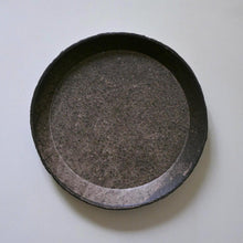Load image into Gallery viewer, A round, shallow dark ceramic dish or tray with a textured, speckled surface, photographed from directly above on a light off-white background.