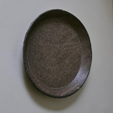Load image into Gallery viewer, A handmade oval ceramic plate or shallow dish with a textured, speckled dark gray and brown glaze, photographed from directly above on a plain off-white background.